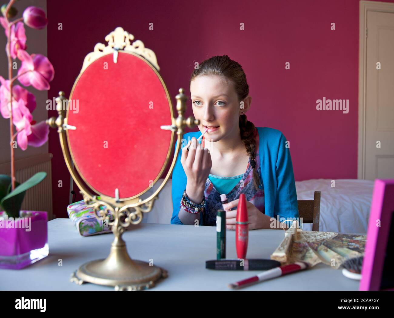 Giovane ragazzina di quattordici anni si siede nella sua camera da letto applicando trucco in uno specchio in preparazione per uscire. Foto Stock