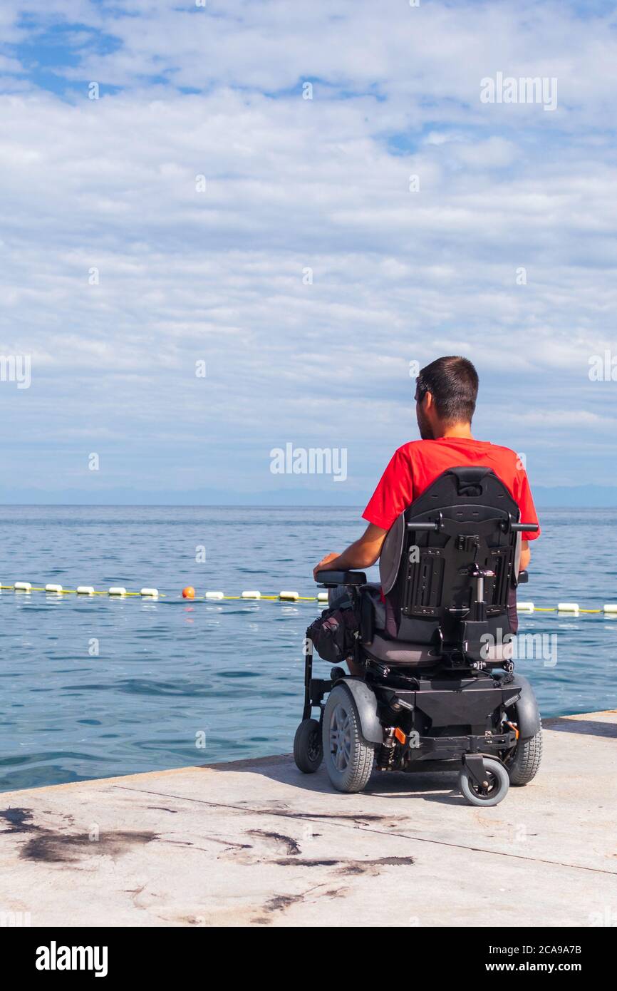 Uomo seduto in sedia a rotelle sulla spiaggia. Pericoli di saltare in acqua da altezze. Lesioni alla testa e alla colonna vertebrale. Foto Stock
