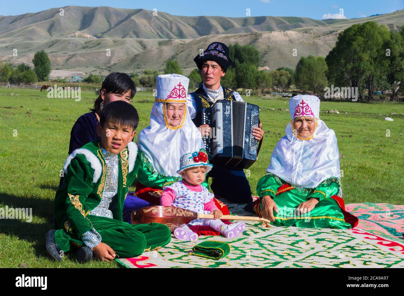 Famiglia kazako in abiti tradizionali ascoltando la musica di un fisarmonicista per solo uso editoriale, Sati village, Tien Shan montagne, kazaki Foto Stock