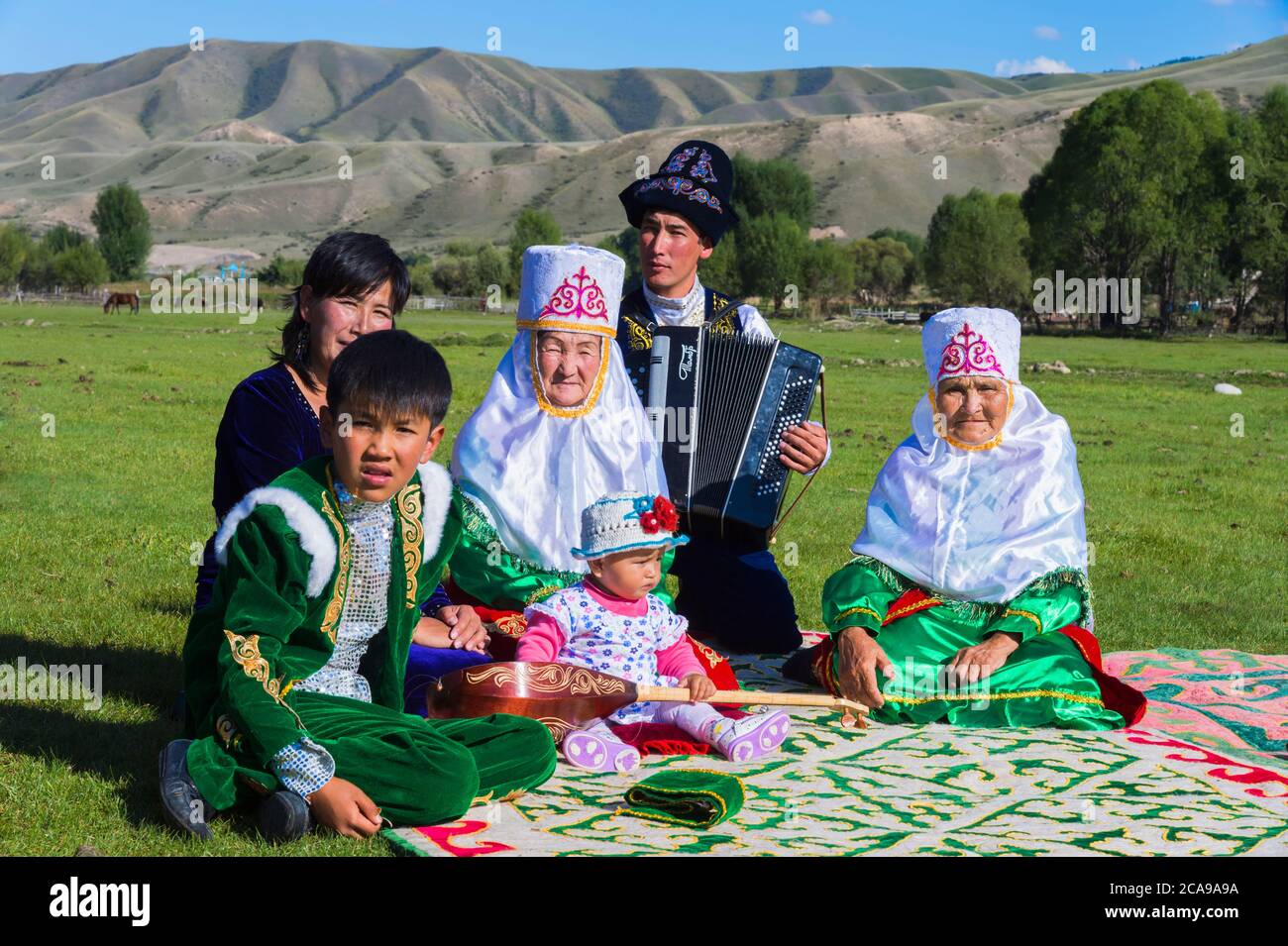 Famiglia kazako in abiti tradizionali ascoltando la musica di un fisarmonicista per solo uso editoriale, Sati village, Tien Shan montagne, kazaki Foto Stock