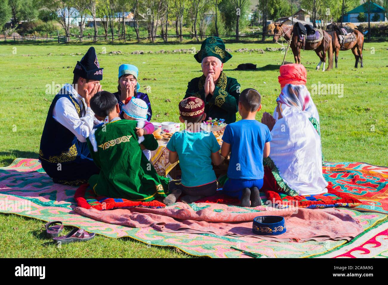 Famiglia kazako in abiti tradizionali pregare prima di pranzo, per il solo uso editoriale, Sati village, Tien Shan montagne, Kazakistan Foto Stock