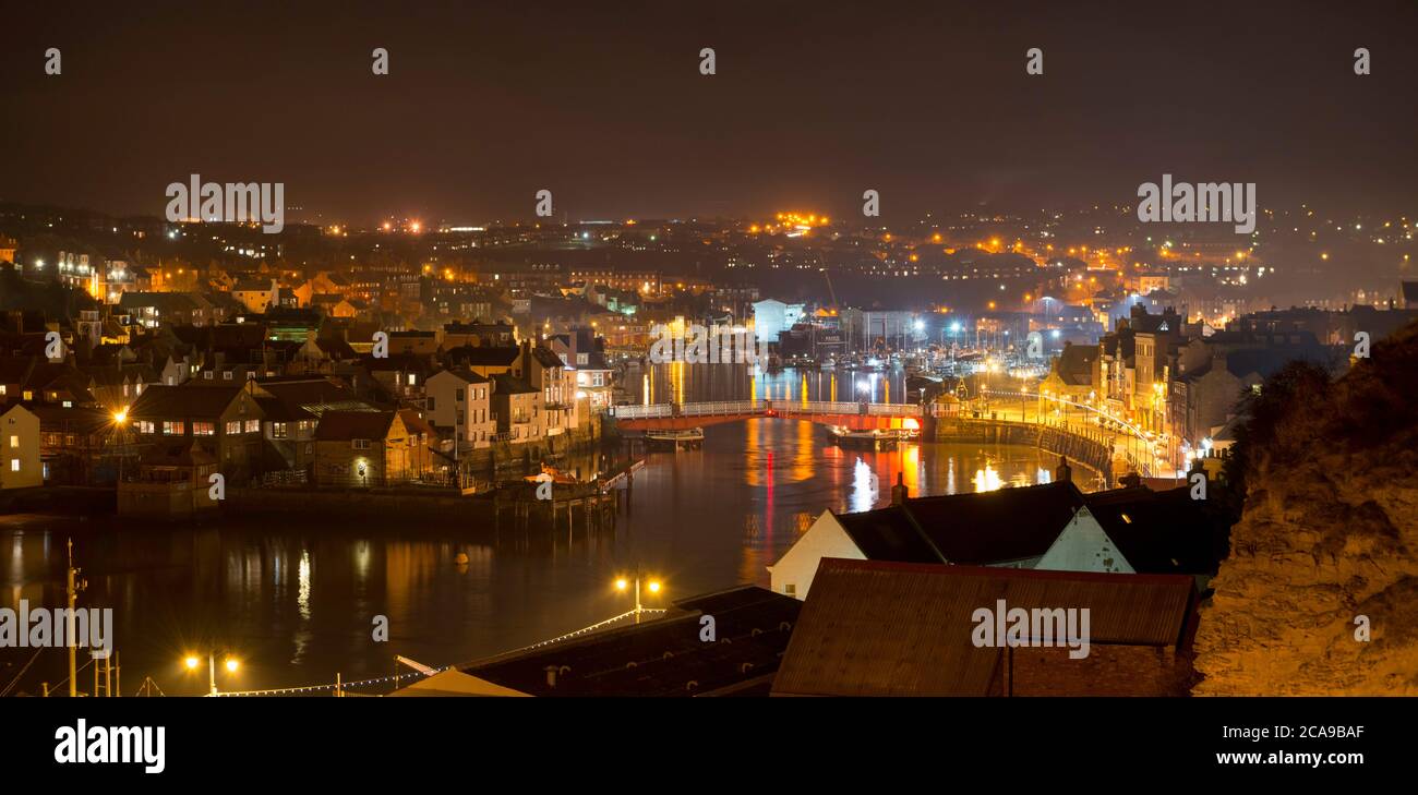 Vista notturna dello storico ponte sospeso e del fiume ESK illuminato dalle luci della città di Whitby Foto Stock