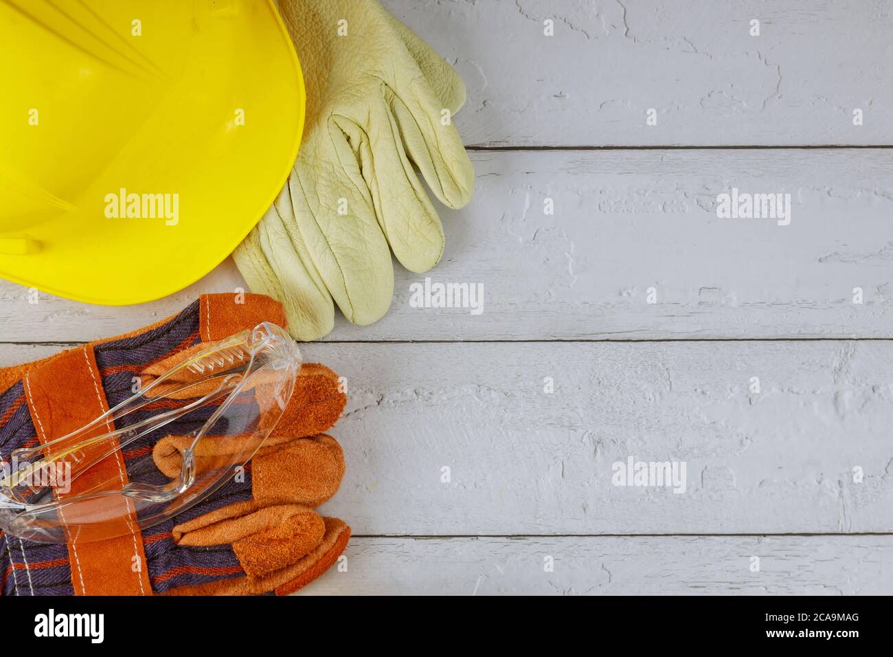 Costruzione attrezzatura di sicurezza sul lavoro con elmetto elmetto giallo e un paio di guanti da lavoro occhiali di sicurezza su fondo bianco di legno Foto Stock