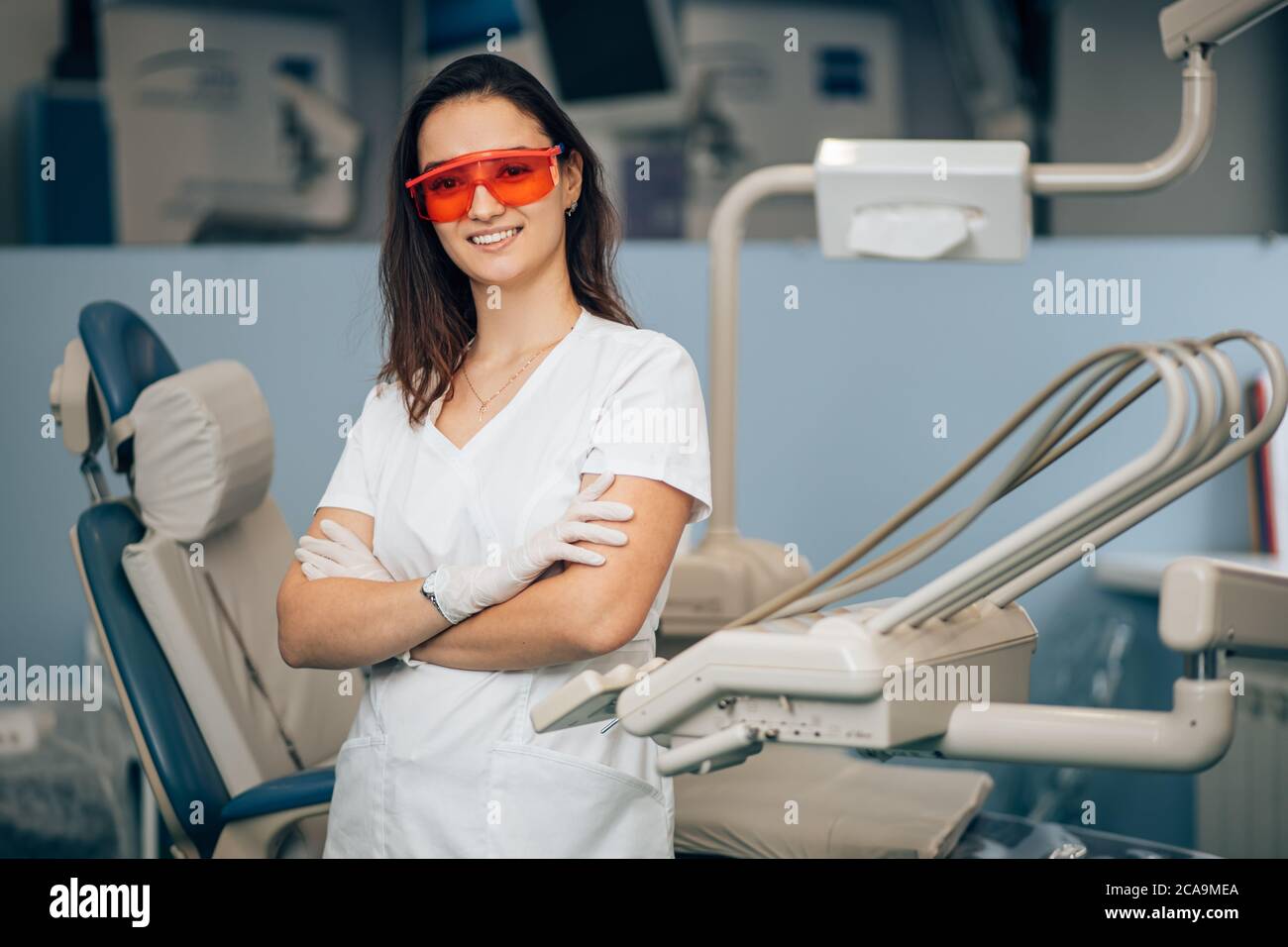 ritratto di dentista donna in uniforme del medico bianco in piedi in ufficio vicino all'attrezzatura e guardare la macchina fotografica, indossando occhiali rossi per la sicurezza. Medicina, Foto Stock