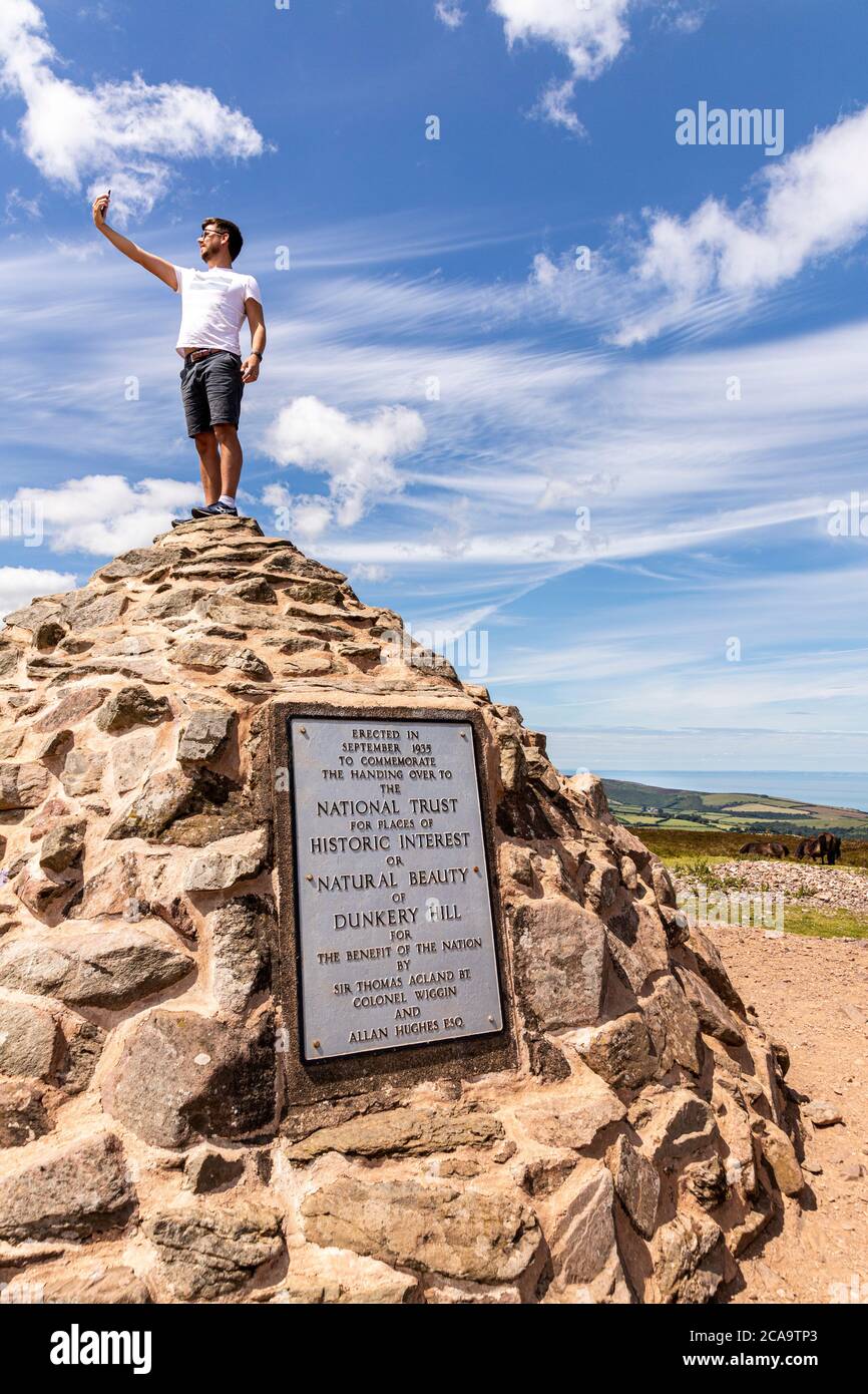Exmoor National Park - un giovane uomo che prende un selfie sulla cima della cairn che segna il punto più alto su Exmoor, Dunkery Beacon, Somerset UK Foto Stock