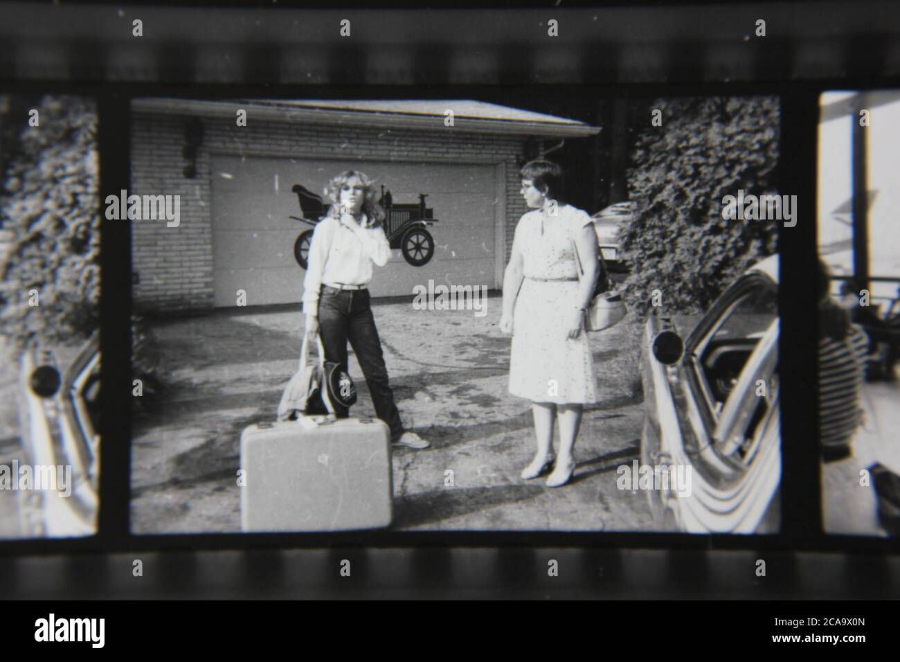 Bella fotografia in bianco e nero d'epoca degli anni '70 di una famiglia che dice i loro goodbyes sul vialetto della casa di famiglia. Foto Stock