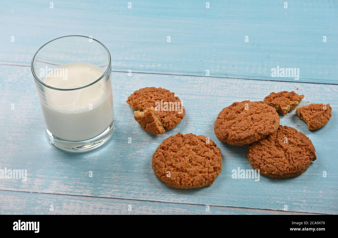 Primo piano diversi biscotti d'avena artigianali rotondi e un bicchiere di latte su un tavolo in legno rustico dipinto di blu, vista ad angolo alto Foto Stock