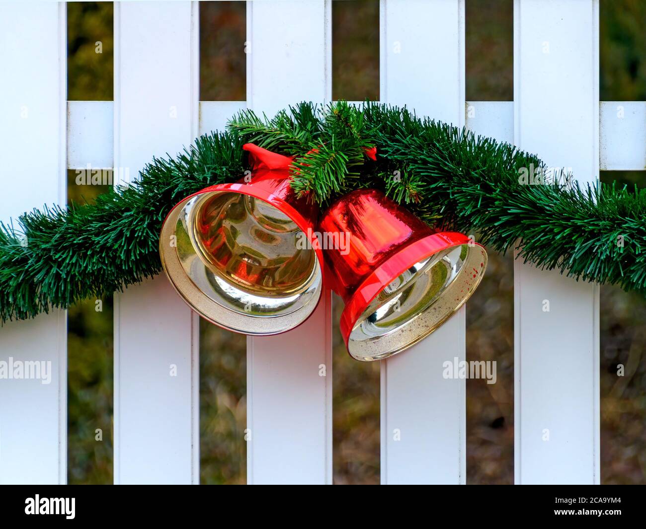 Recinzione bianca con decorazione natalizia realizzata da una ghirlanda verde e due campane lucide metalliche rosse Foto Stock