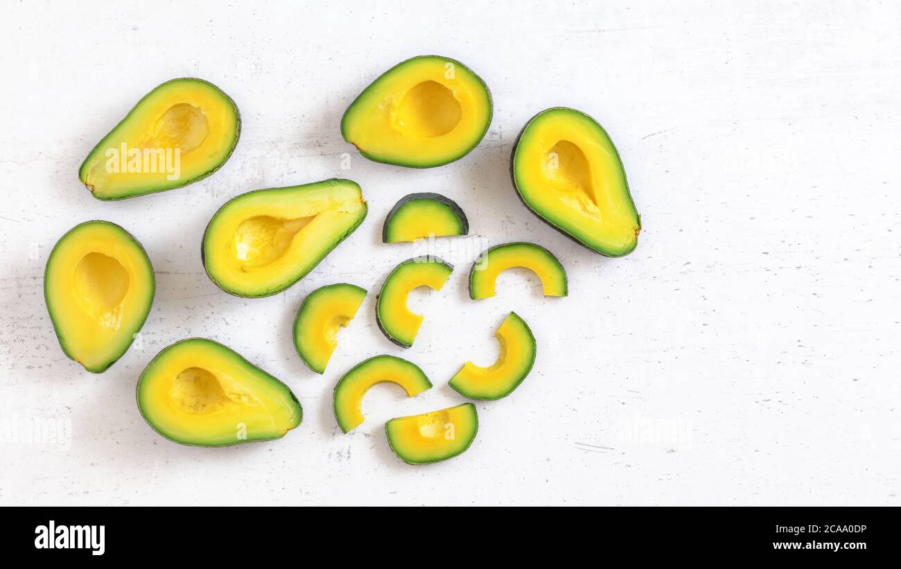 Vista dall'alto, metà avocado e fette, su tavola da lavoro bianca, la polpa di frutta ha un colore verde e giallo vivace, spazio per il testo a destra. Foto Stock