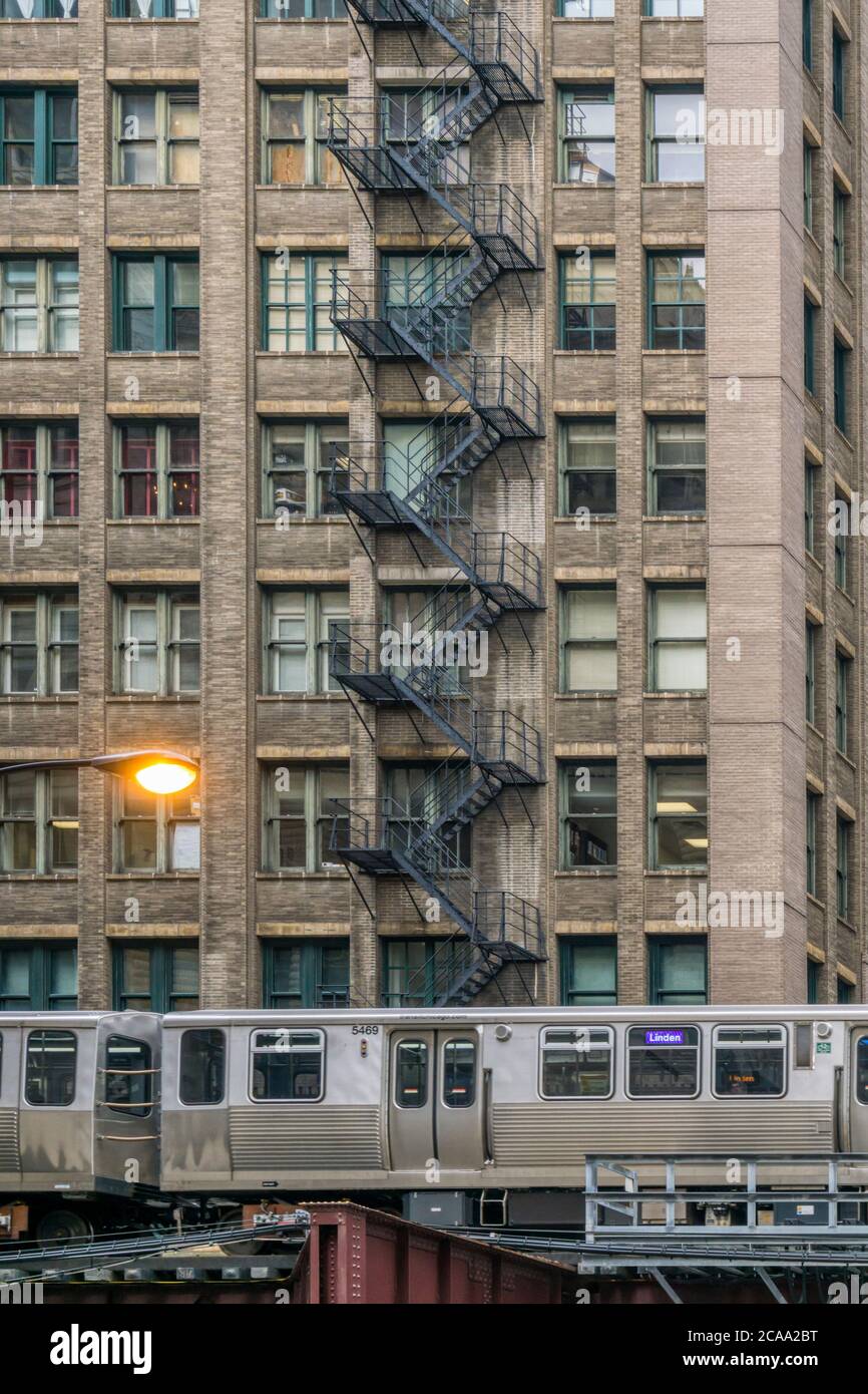 Il treno Chicago El passa davanti ad un alto edificio commerciale con un'uscita esterna in metallo. Foto Stock