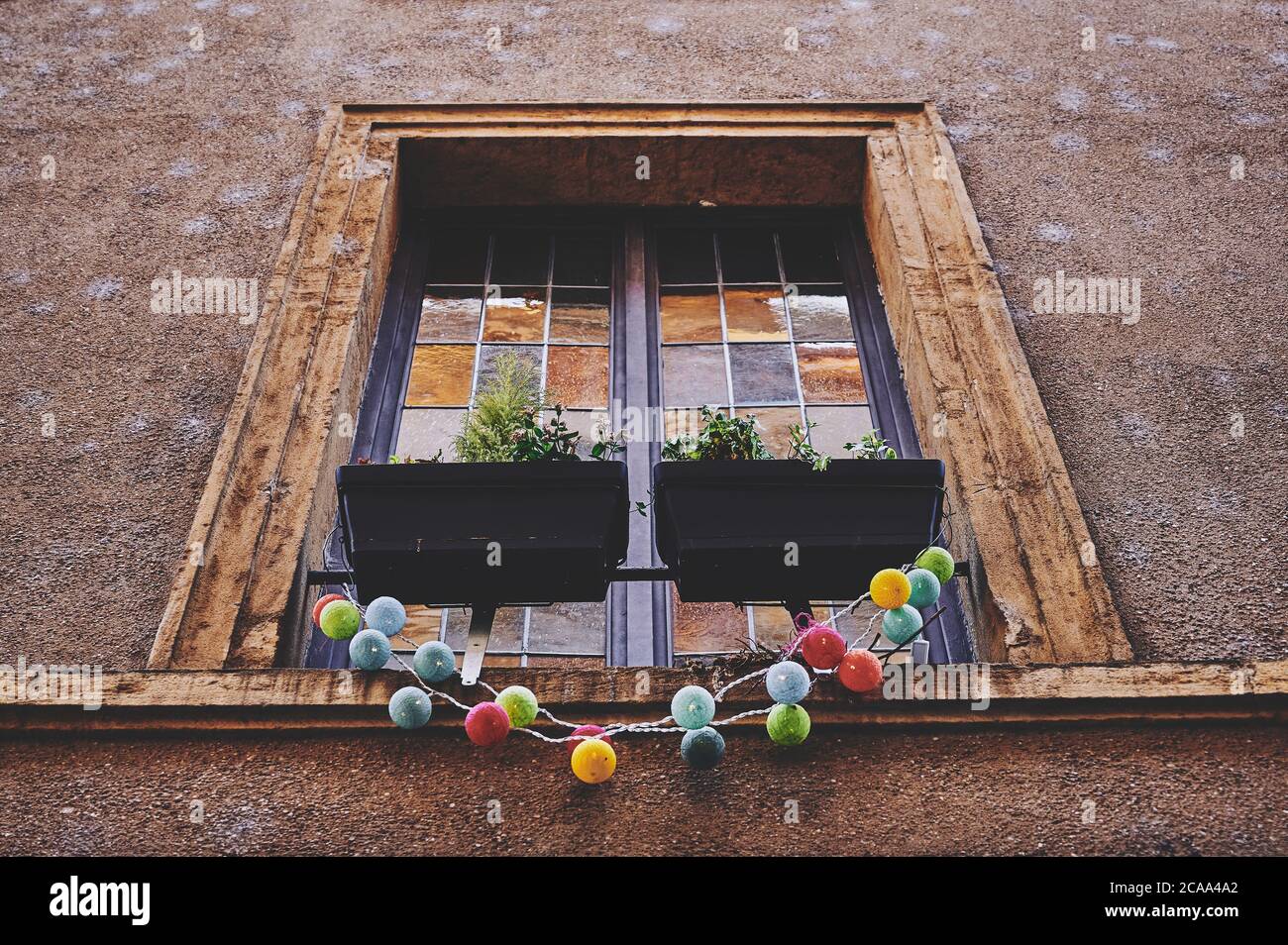 Una vecchia finestra francese con piastrelle di vetro colorate e davanzale in legno, catena di luce colorata vi pende Foto Stock