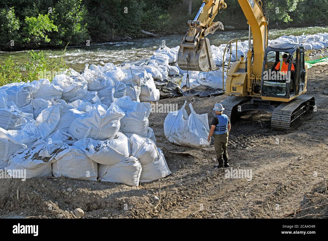 Un equipaggio di costruzione di mitigazione delle inondazioni che utilizza un escavatore per sollevare pesanti sacchi di roccia per stabilizzare le rive del fiume Elbow, Calgary Canada Foto Stock