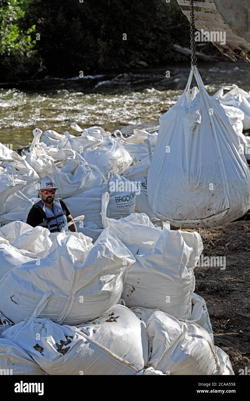 Un equipaggio di costruzione di mitigazione delle inondazioni che utilizza un escavatore per sollevare pesanti sacchi di roccia per stabilizzare le rive del fiume Elbow, Calgary Canada Foto Stock