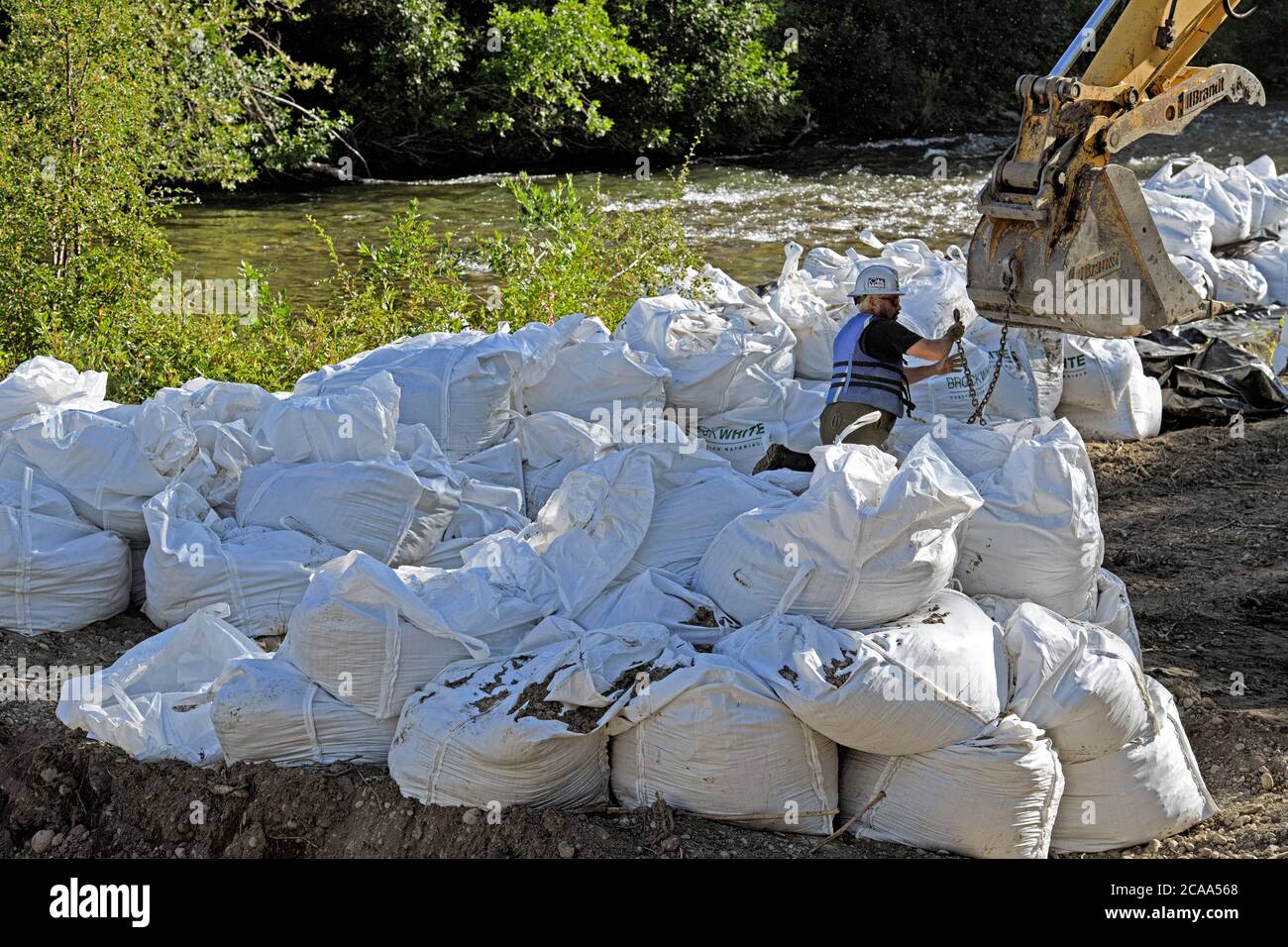 Un equipaggio di costruzione di mitigazione delle inondazioni che utilizza un escavatore per sollevare pesanti sacchi di roccia per stabilizzare le rive del fiume Elbow, Calgary Canada Foto Stock