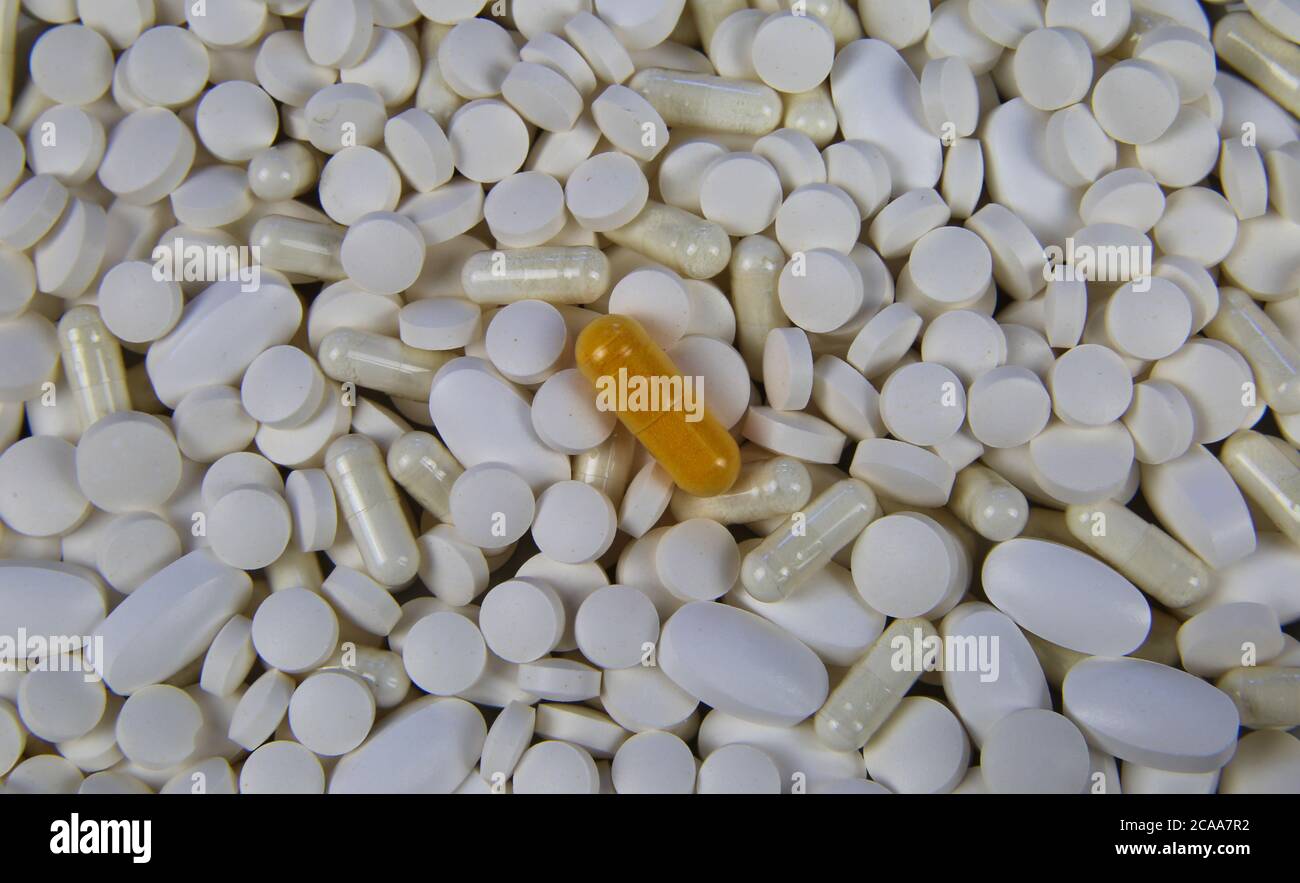 Closeup full frame di pile innumerevoli pillole bianche e capsule con una capsula gialla al centro (concentrarsi sulla pillola gialla) Foto Stock