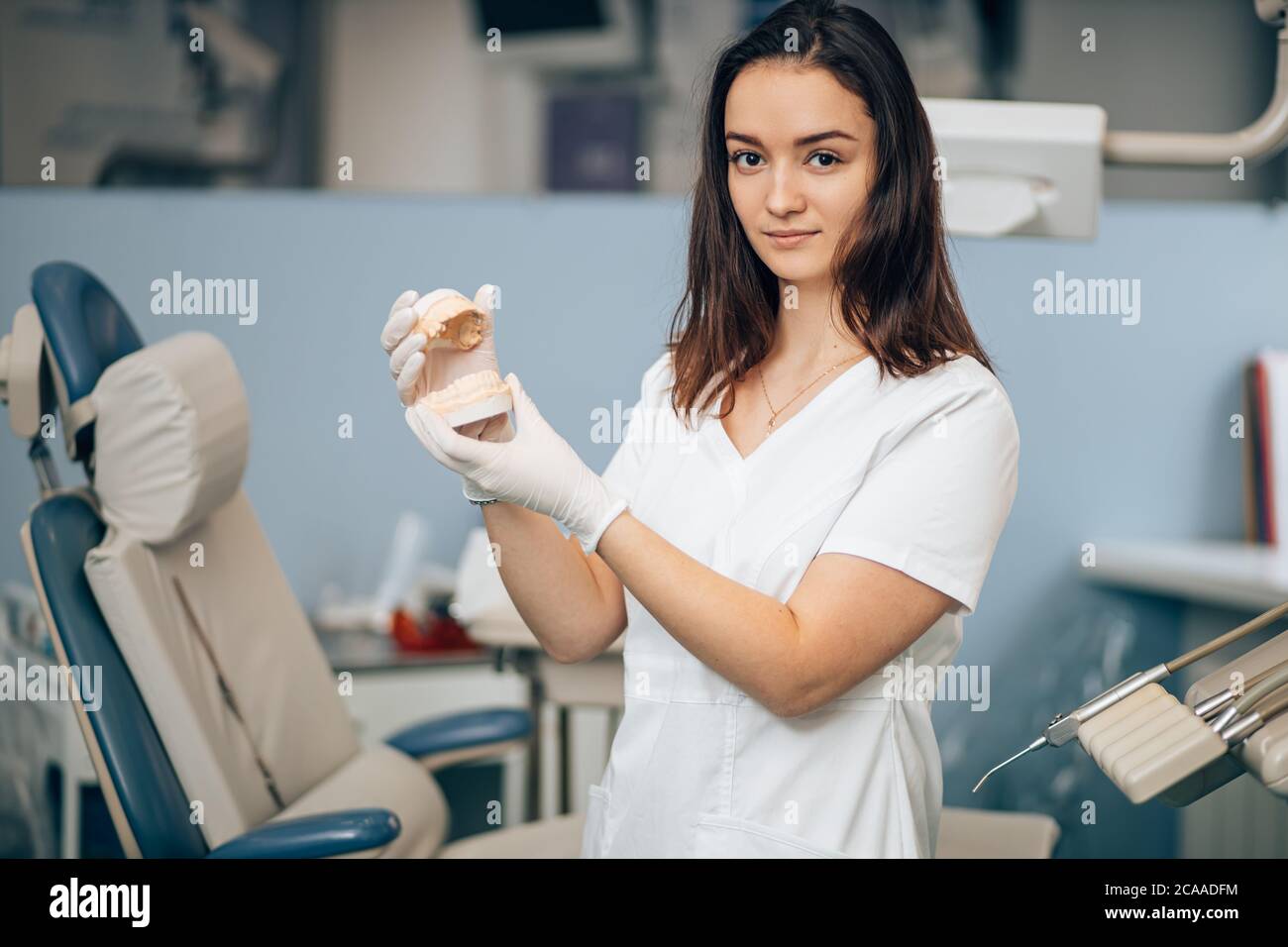 ritratto di dentista al lavoro, indossando l'uniforme bianca del medico, utilizzando strumenti e attrezzature mediche, tenendo in mano la protesi. Healthcar Foto Stock