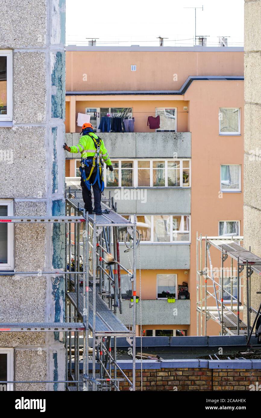 l'operaio monta il ponteggio sulla facciata di una casa a più piani ad un'altezza pericolosa Foto Stock