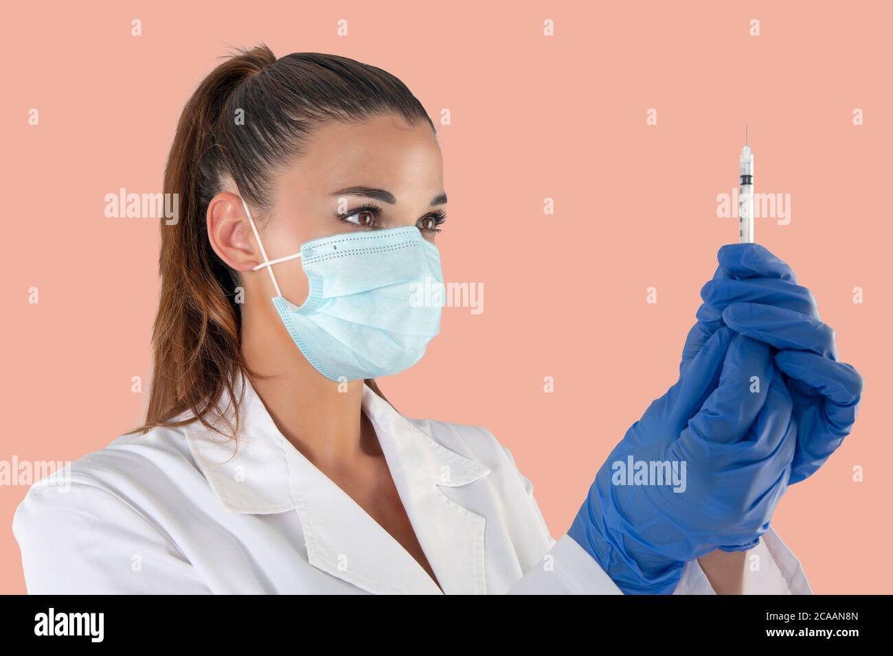 Attraente medico femminile che indossa una maschera anti-virus e guanti in lattice con una siringa di vaccino. Foto Stock