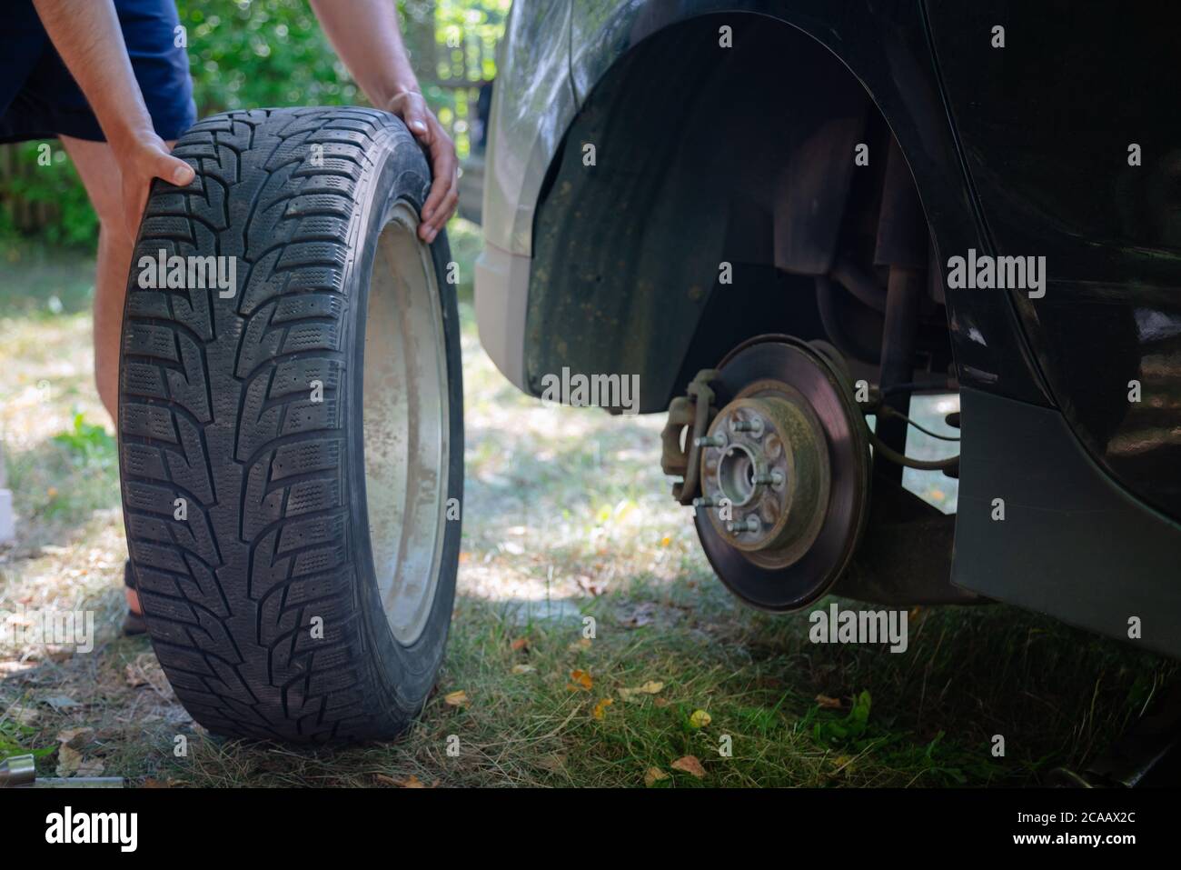 Primo piano delle mani maschili che cambiano il pneumatico dell'auto all'esterno. Sostituzione pneumatico del veicolo rotto sull'erba. Incidente di viaggio. Foto Stock