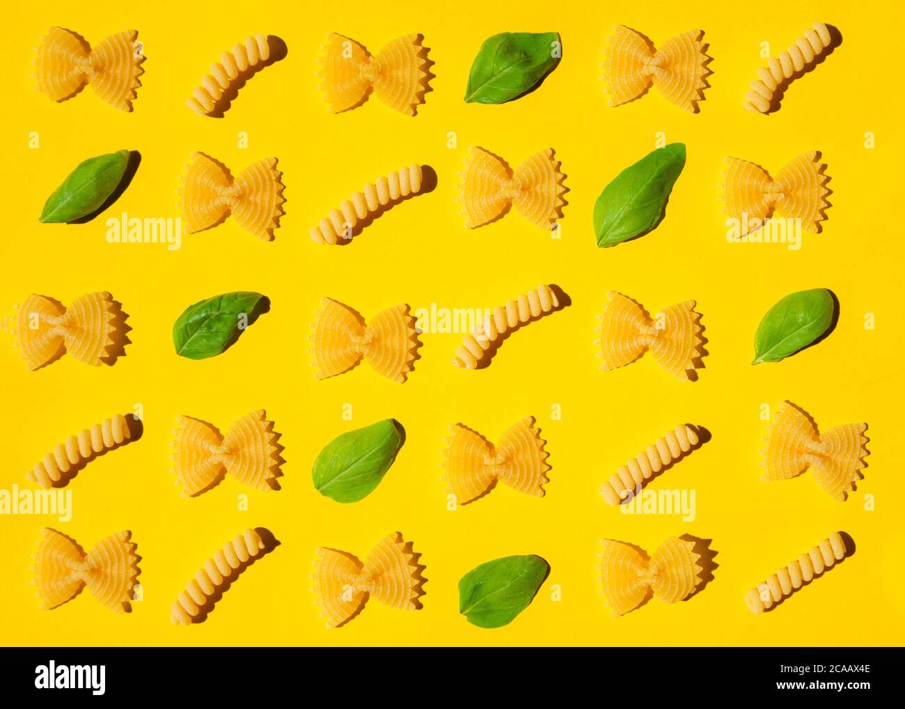 Pasta arricciata e foglie di basilico non cotti su sfondo giallo. Tradizionale modello di maccheroni crudi asciutti. Nessuno Foto Stock