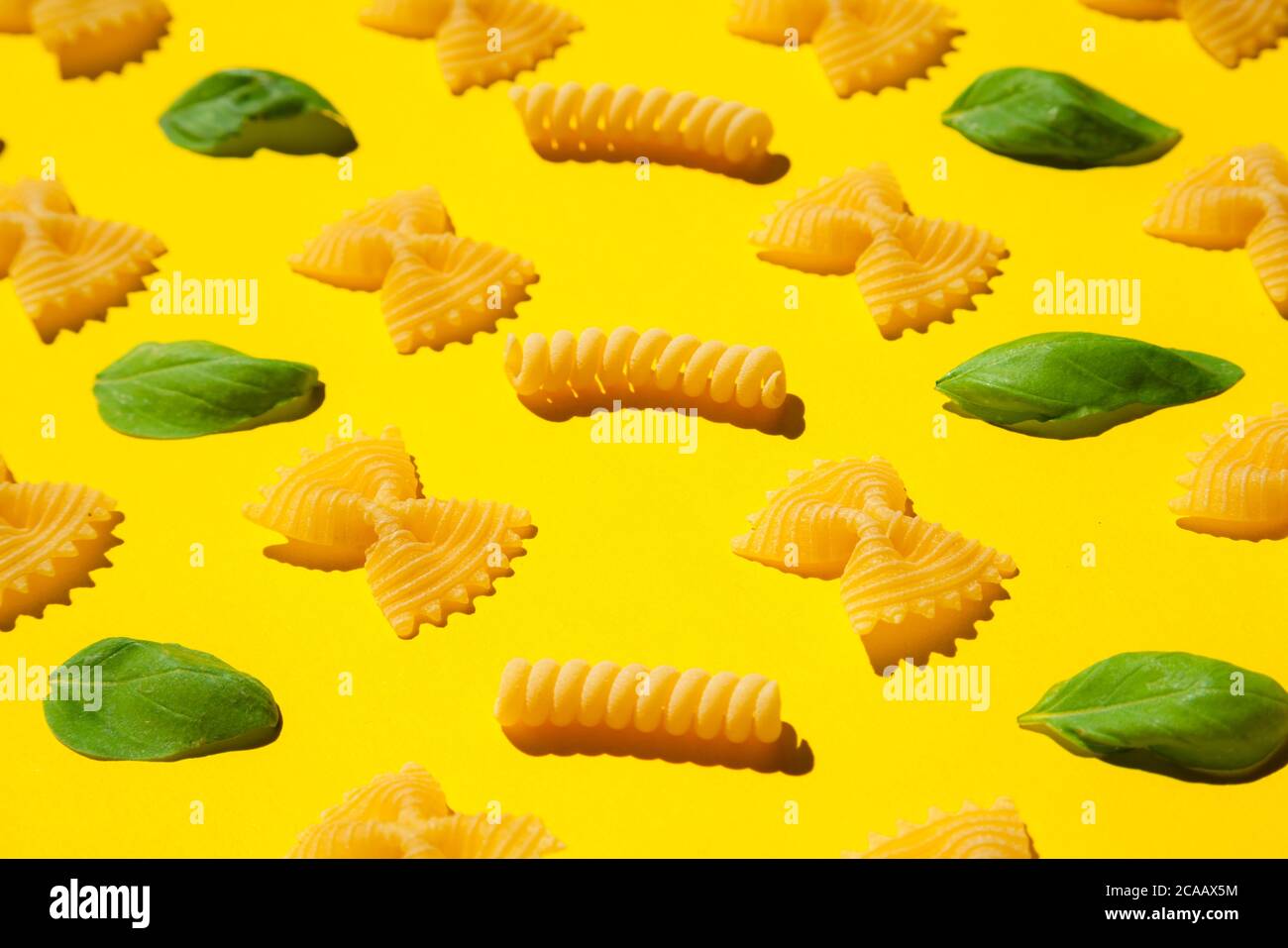 Pasta arricciata e foglie di basilico non cotti su sfondo giallo. Tradizionale modello di maccheroni crudi asciutti. Nessuno Foto Stock