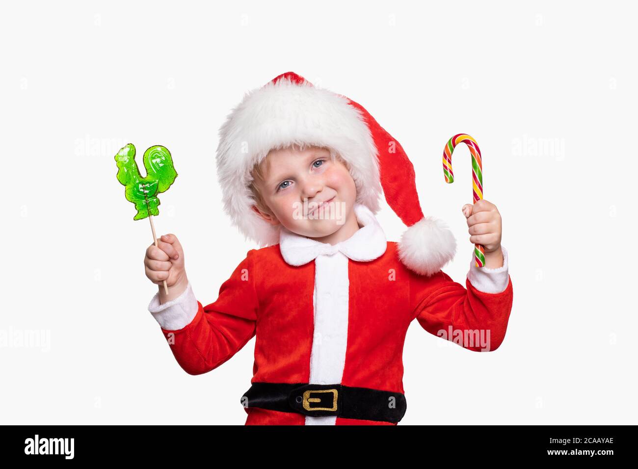 Un bambino di 4 anni in un costume di Capodanno e un cappello di Babbo Natale tiene le caramelle nelle sue mani. Allegro positivo gioioso concetto di vacanza e. Foto Stock