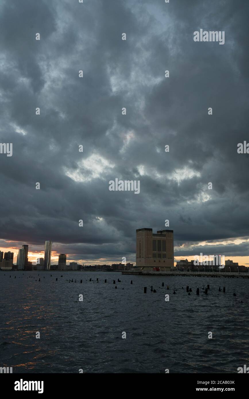 Mentre la tempesta tropicale Isaias cominciò a passare fuori dalla zona di New York lasciando un sentiero di forti venti, il sole tramonta sul fiume Hudson e Jersey City Foto Stock