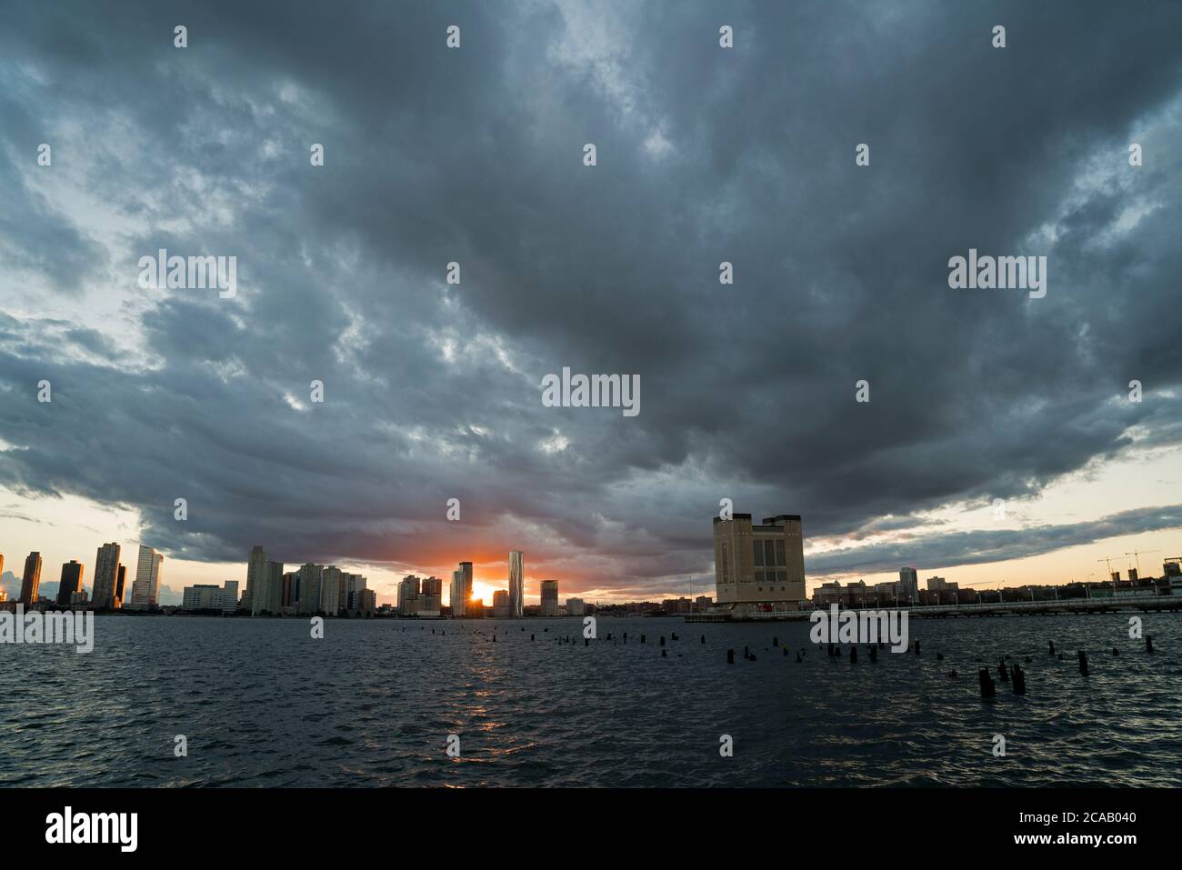 Mentre la tempesta tropicale Isaias cominciò a passare fuori dalla zona di New York lasciando un sentiero di forti venti, il sole tramonta sul fiume Hudson e Jersey City Foto Stock