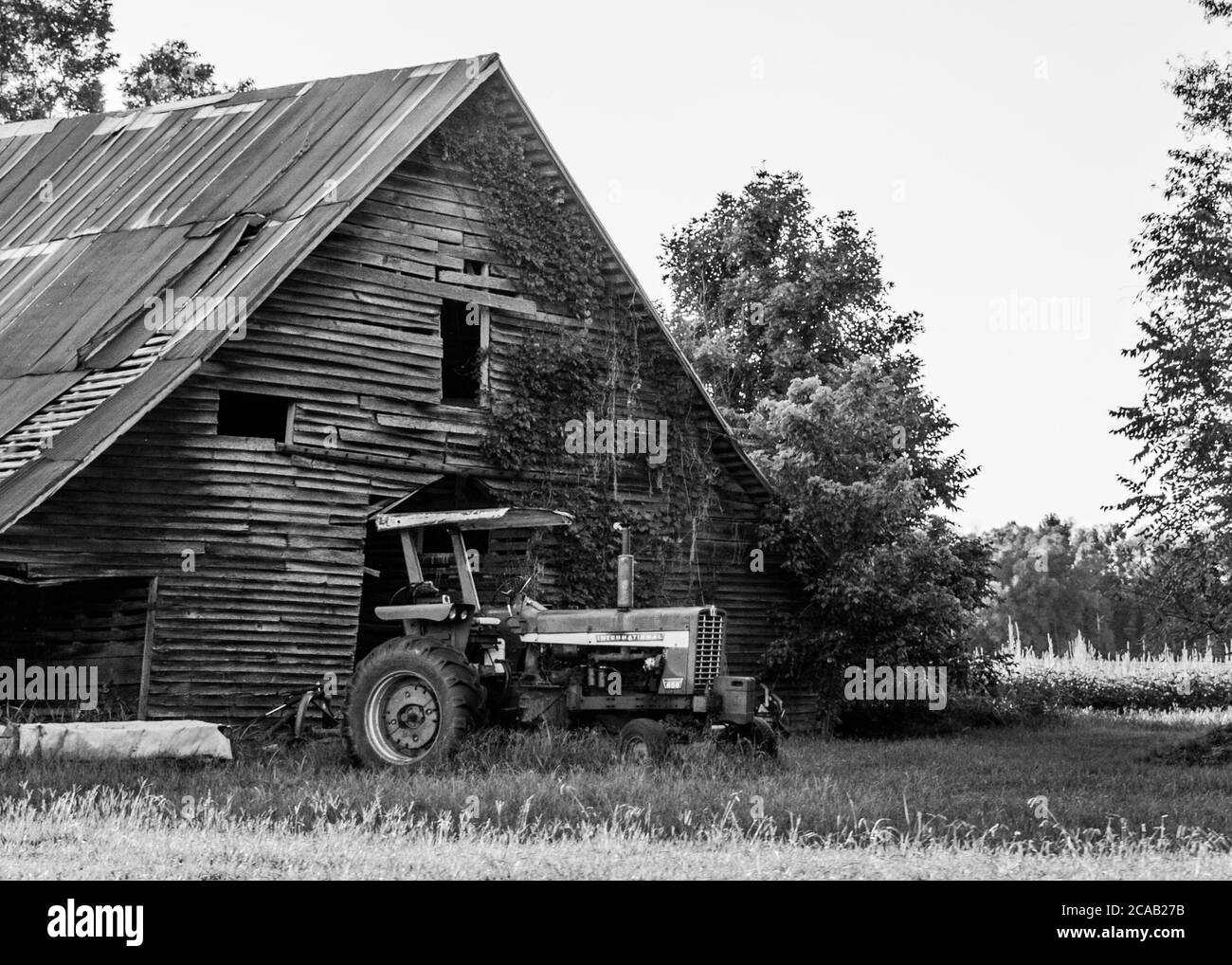 Un vecchio, rustico, e rundown fienile con un trattore in bianco e nero Foto Stock