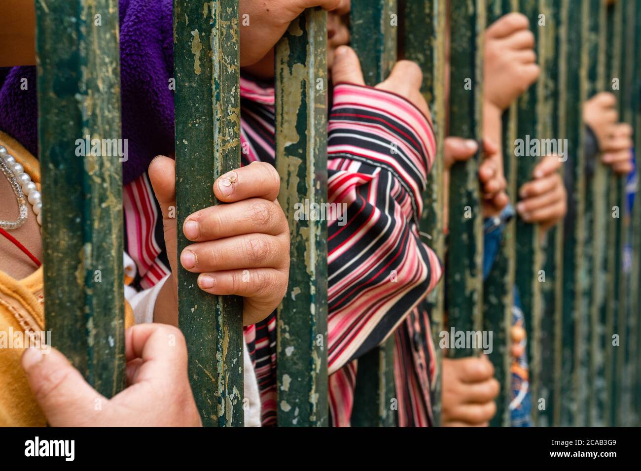 Un gruppo di bambini si affligge alle sbarre metalliche: Si applicano i concetti di sfruttamento dei minori, immigrazione, abuso, tratta di esseri umani, sofferenza Foto Stock