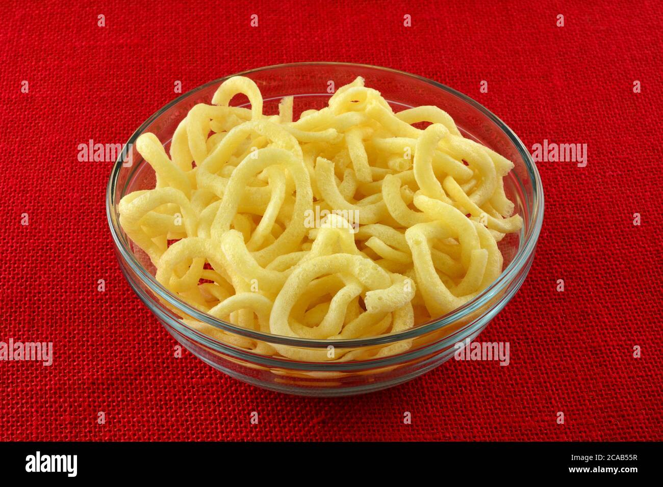 Gli anelli di cipolla lievemente fritti si snodano in una ciotola di vetro su una tovaglia rossa Foto Stock