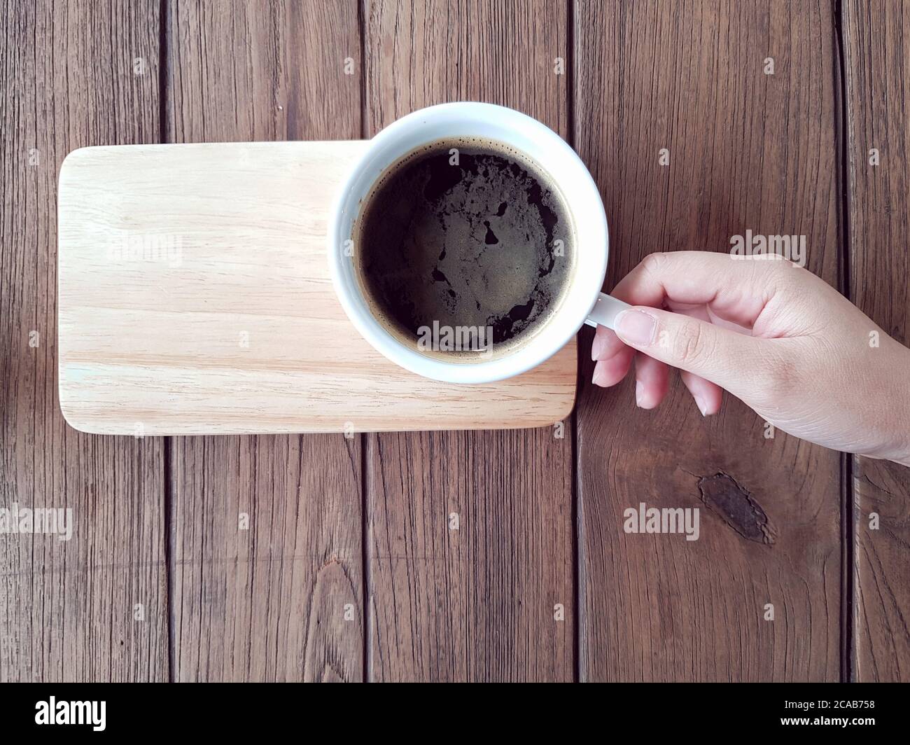 Mano che tiene il caffè nero su tavola di legno Foto Stock