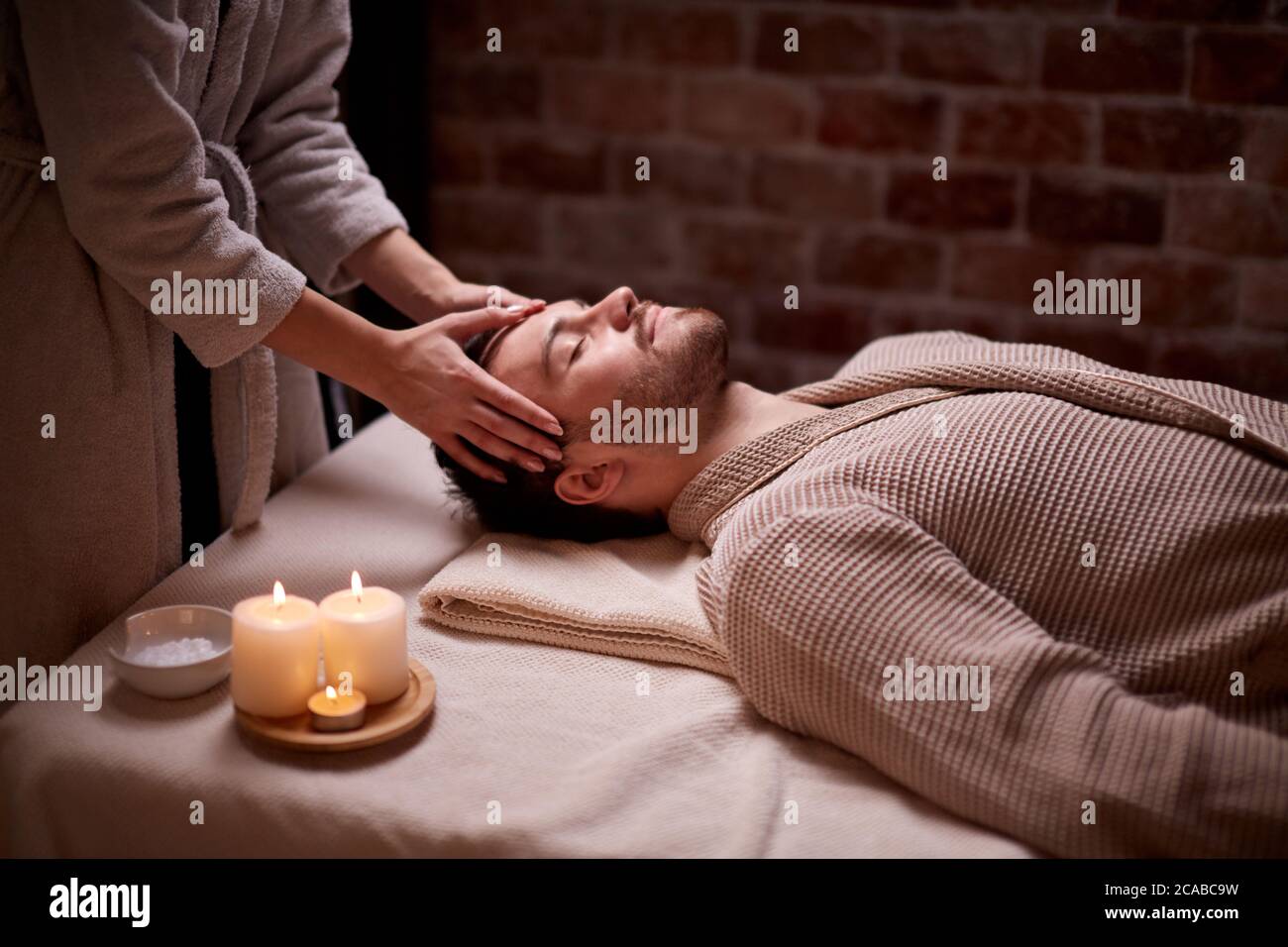 Salone di bellezza, concetto di trattamento. Giovane uomo caucasico ottenere massaggio su testa e viso sdraiato sulla scrivania con gli occhi chiusi, calma Foto Stock