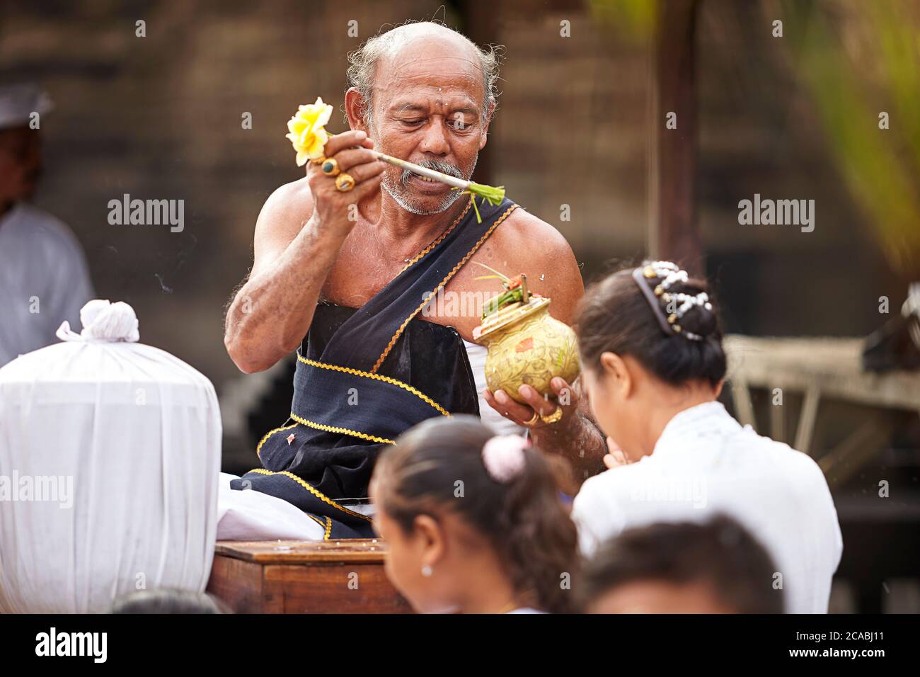 Un leader della cerimonia religiosa indù balinese spruzzi acqua sul le donne partecipanti per purificarsi e iniziare la cerimonia Foto Stock