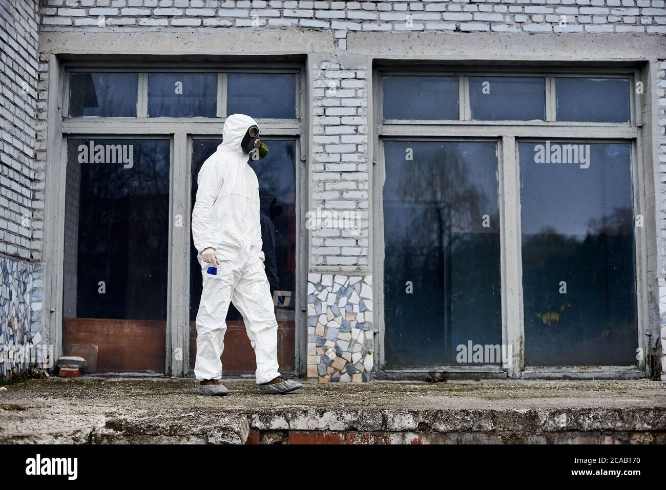 Intera lunghezza dell'ambientalista maschile in matraccio di tenuta per tuta radioattiva con liquido blu. Ricercatore che indossa tuta protettiva bianca, maschera a gas, copriscarpe. Concetto di ecologia e inquinamento ambientale. Foto Stock