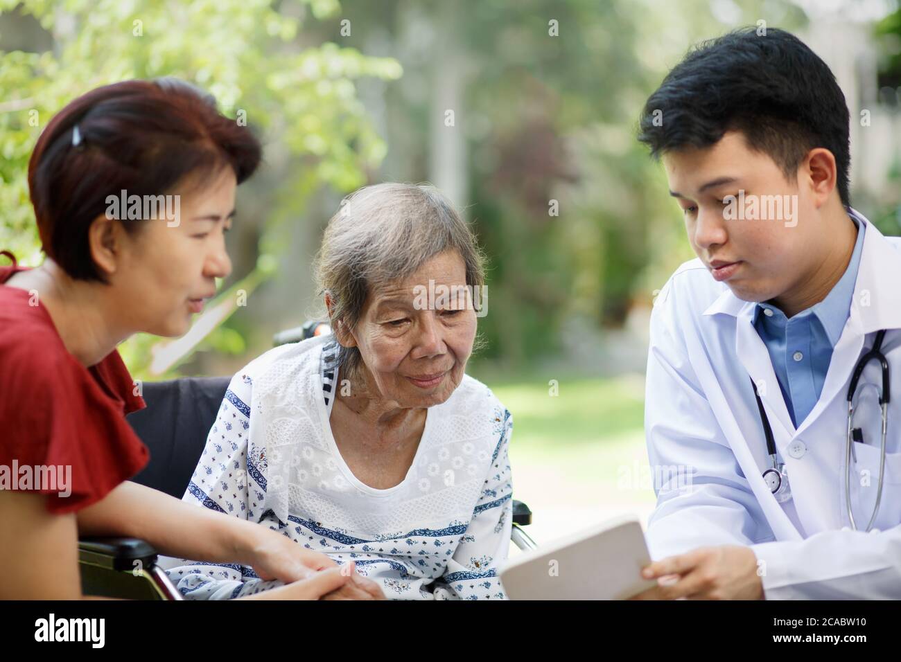 Medico asiatico che parla con la paziente anziana su sedia a rotelle Foto Stock