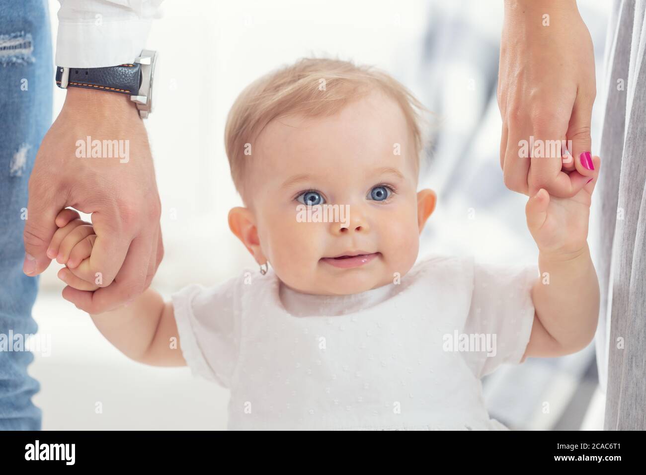 Aspetto innocente di una bambina dagli occhi blu che tiene la mamma e le mani del papà. Foto Stock