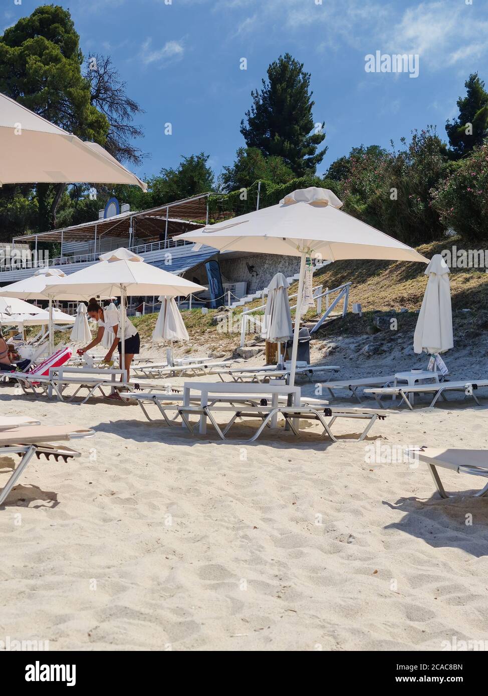 CHALKIDIKI, Grecia - Luglio 30 2020: Pulizia efficace Beach bar solarium mobili per ridurre il rischio di infezioni covid-19. Applicazione di una soluzione disinfettante sulla superficie delle sedie da spiaggia per eliminare germi e batteri. Foto Stock
