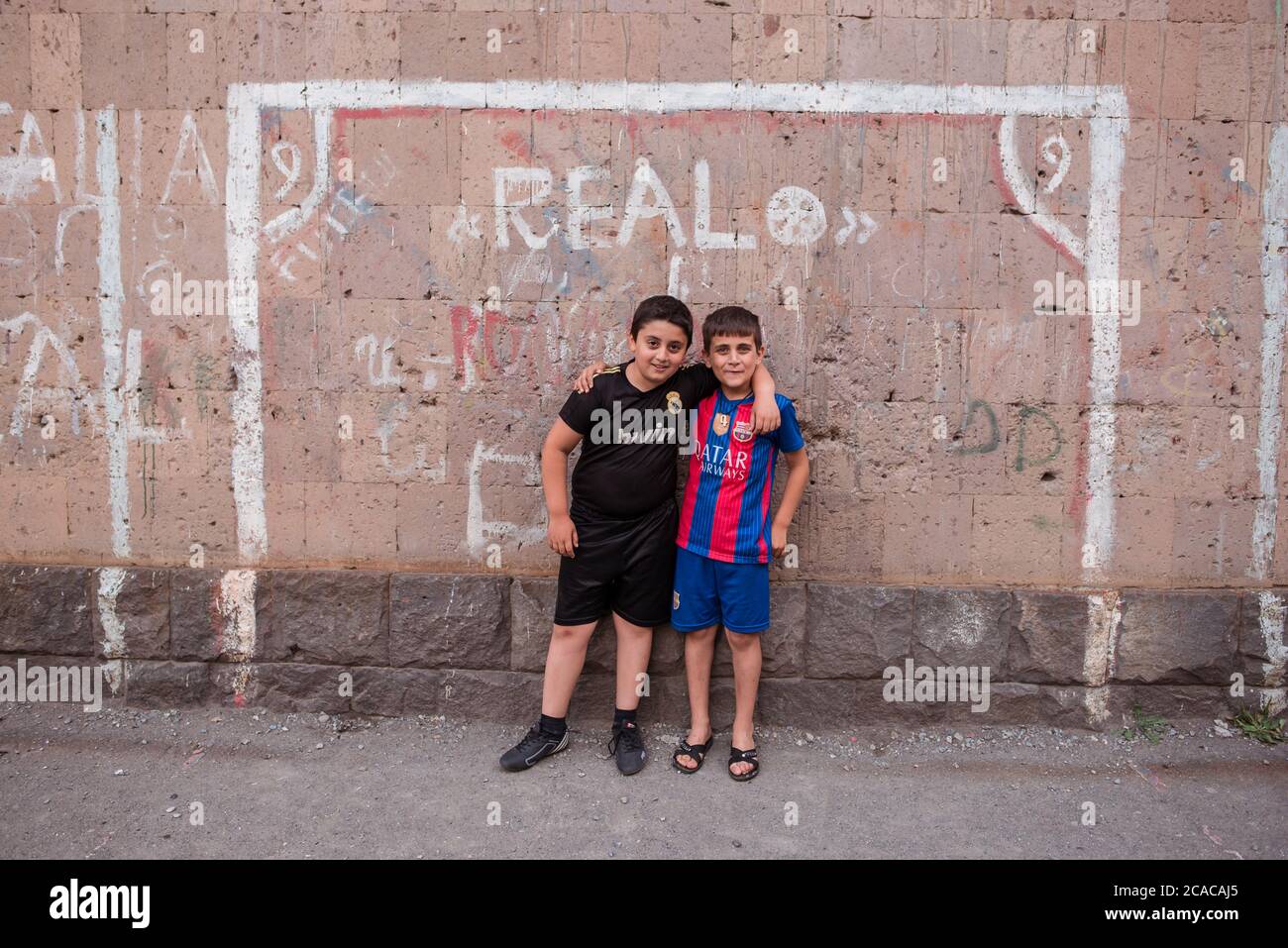 Alaverdi / Armenia - 20 luglio 2019: Amici bambini con camicie di squadre rivali Real Madrid e FC Barcellona in posa davanti al calcio obiettivo dipinto su muro Foto Stock