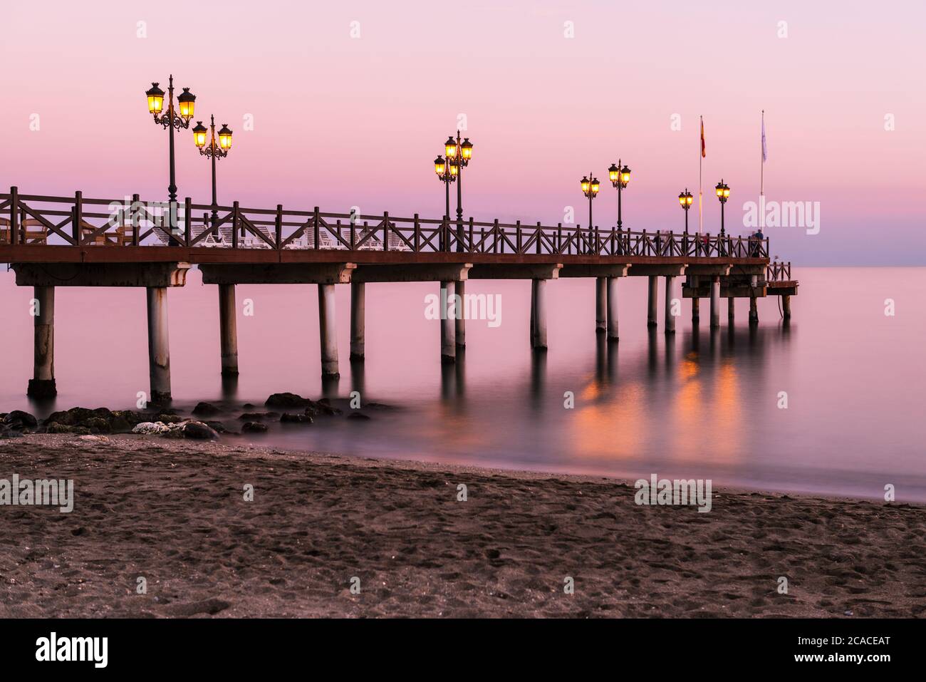 Molo illuminato in legno su una spiaggia di Marbella durante il tramonto. Esposizione lunga. Foto Stock