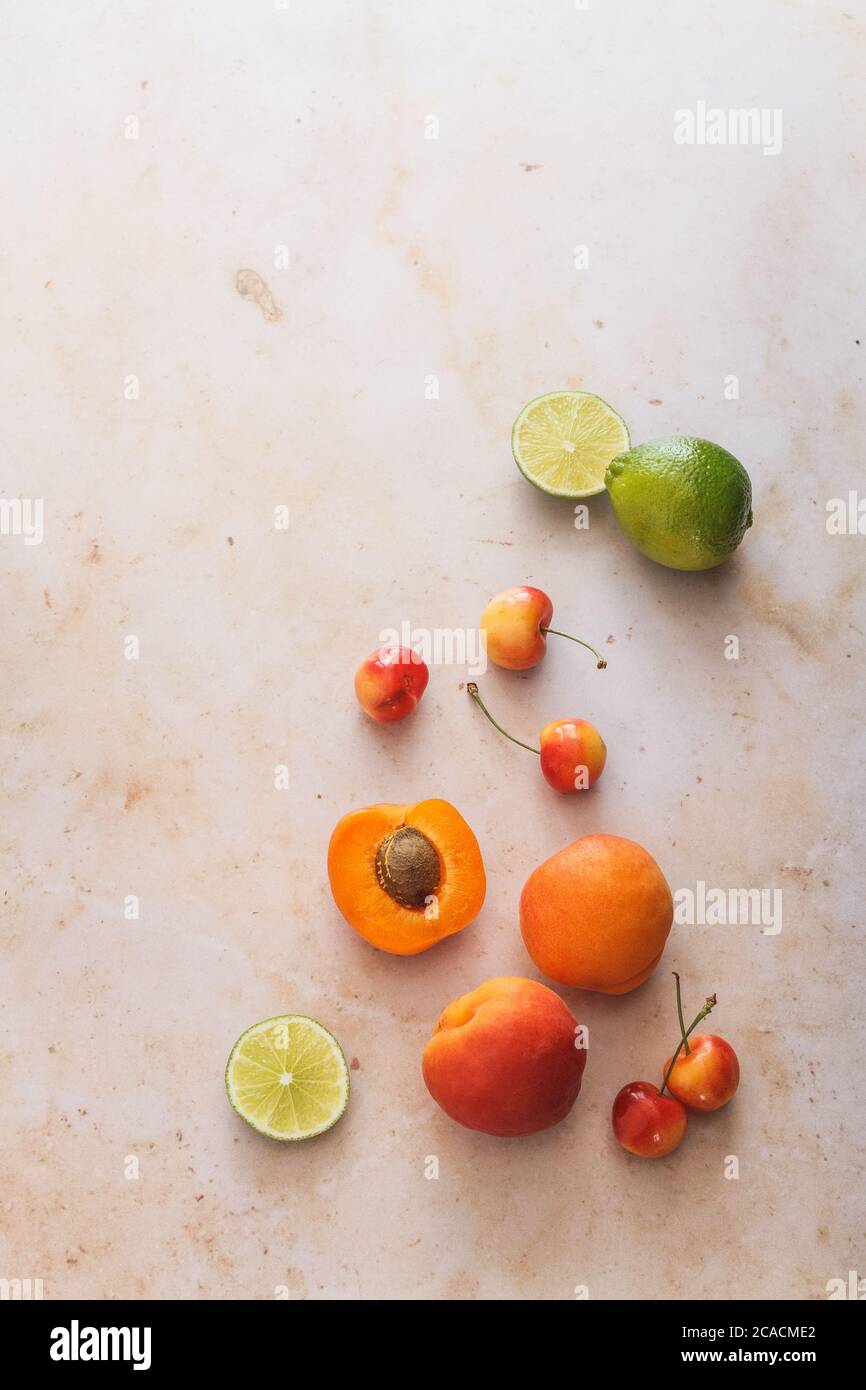 Frutta estiva sana. Albicocche, ciliegie e lime su uno sfondo di marmo rosa. Foto Stock