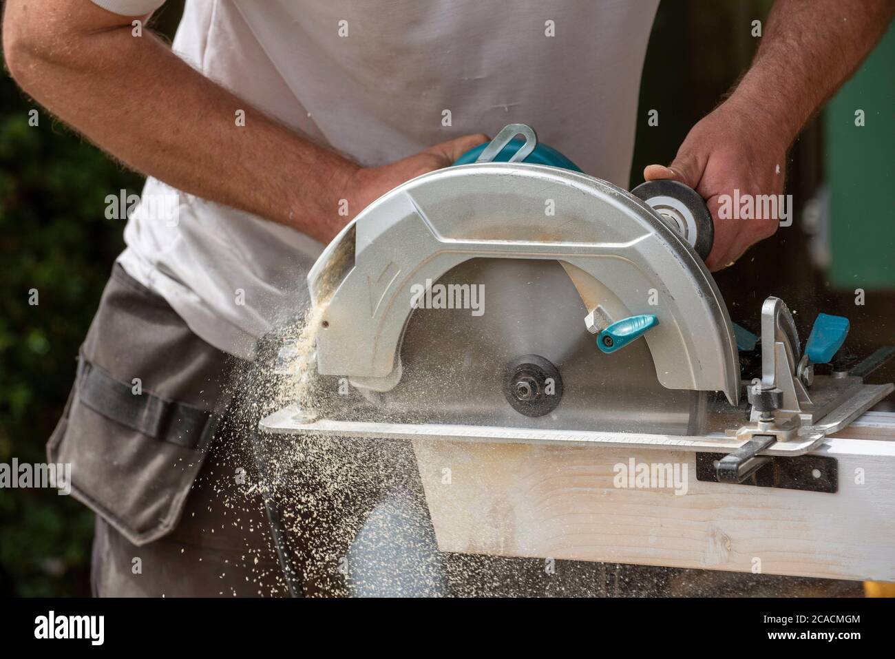 Hampshire, Inghilterra, Regno Unito. 2020. Carpentiere che tiene una sega circolare per tagliare una tavola di legno che crea una polvere di legno fine. Foto Stock