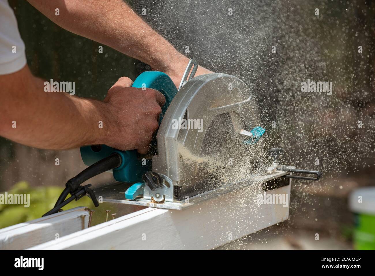 Hampshire, Inghilterra, Regno Unito. 2020. Carpentiere che tiene una sega circolare per tagliare una tavola di legno che crea una polvere di legno fine. Foto Stock