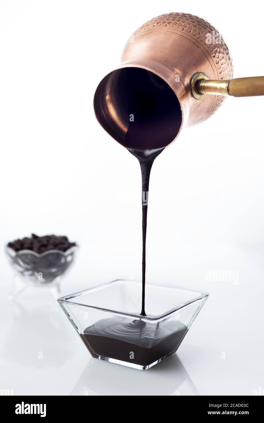 Colpo verticale di uno sciroppo di cioccolato che è versato giù da una pentola di cezve su una ciotola di vetro Foto Stock