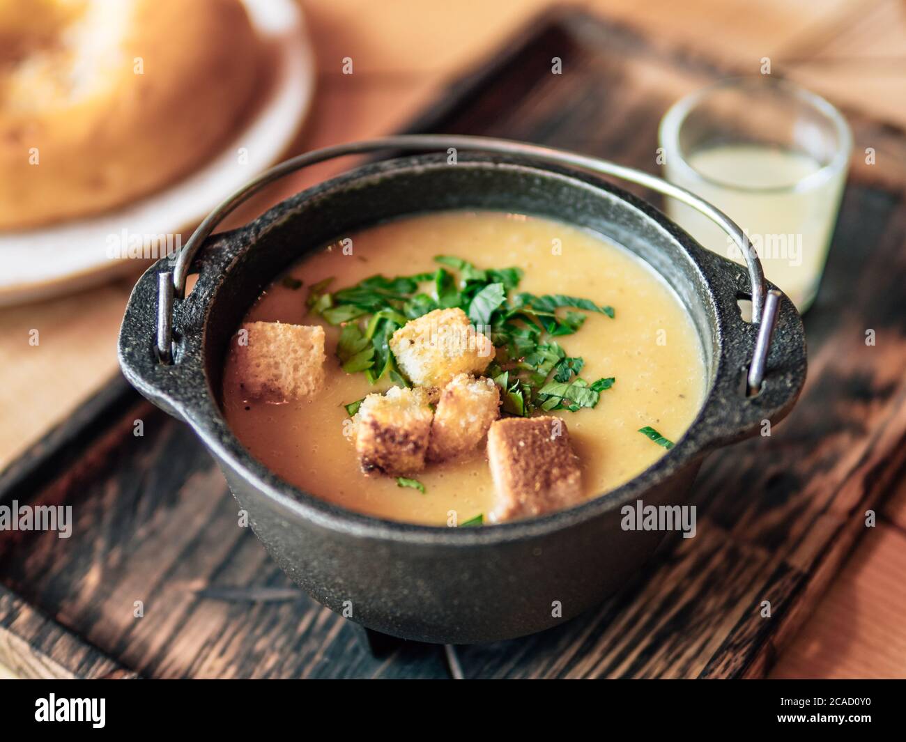 Purea zuppa con crostini e prezzemolo verde in vecchio recipiente di metallo su vecchio vassoio di legno autentico shot di zuppa di crema gialla. Foto Stock
