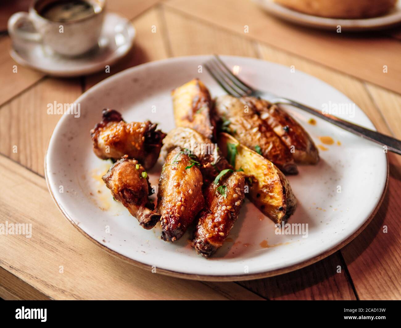 Gustose ali di pollo arrostite e patate arrostite. Autentico shot di piatto con ali di pollo arrostite e patate arrostite su un rustico tavolo in legno. Foto Stock