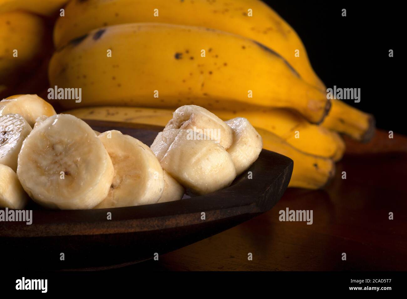 Un mazzo di banane e una banana tagliata in una ciotola su un tavolo Foto Stock