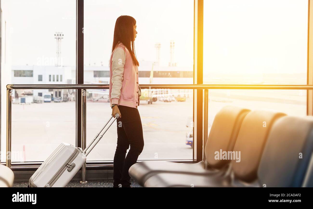 Concetto di stile di vita di viaggio. Donna turistica che aspetta al terminal del cancello d'imbarco prima della partenza con i bagagli che guardano gli aeroplani con vista dell'alba Foto Stock