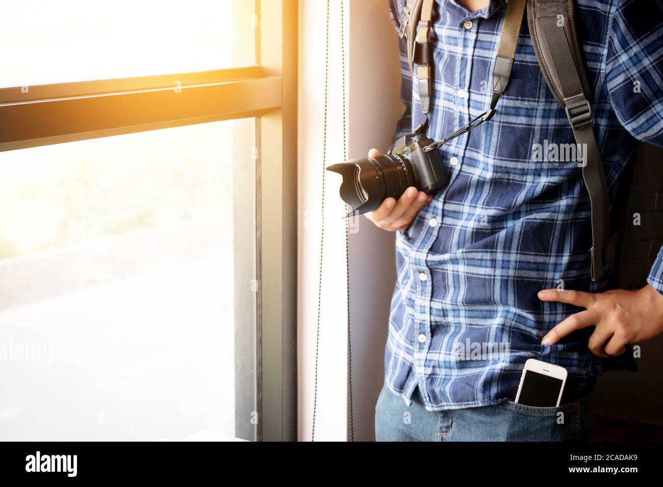 concetto di viaggio e fotografia. fotografo con zaino e fotocamera digitale in piedi vicino alla finestra pronto a viaggiare per scattare foto, volto anonimo. fi Foto Stock