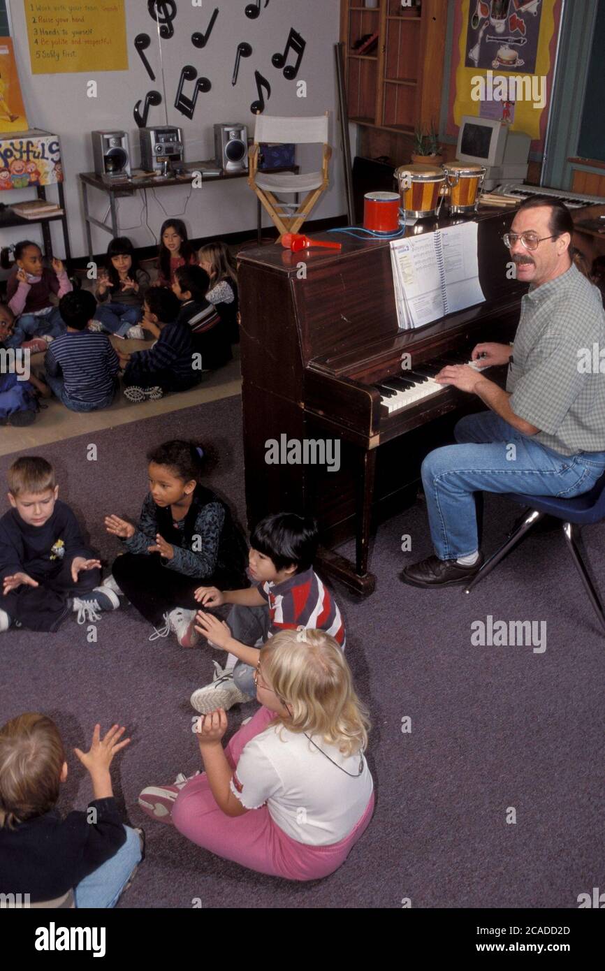 Austin Texas USA, circa 1998: Un insegnante di musica maschile suona il pianoforte canta canzoni con i bambini in un'aula dell'asilo. ©Bob Daemmrich Foto Stock